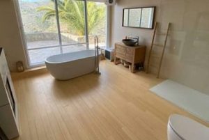 baño con ventanal y bañera a los pies de este. suelo parquet de bambú caramel