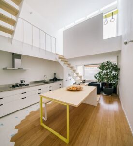 Cocina con suelo de bambú en nuestro modelo vertical caramel, con mesa grande en el centro, encimera blanca a la izquierda y una escalera hacia la planta superior al final de la sala